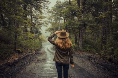 Rear view of woman walking on road in forest