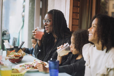 Smiling woman enjoying food and drinks with children while sitting at restaurant