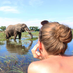 Young woman looking at elephant in water against sky