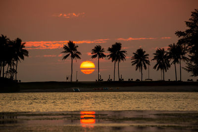 Silhouette palm trees by sea against romantic sky at sunset
