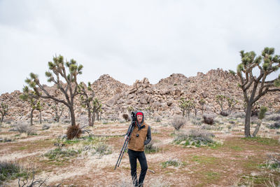 Man with large camera posed in front of boulder piles in desert