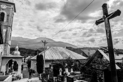 Crucifix by church and houses against cloudy sky