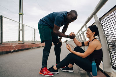 Cheerful male and female athletes holding hands while looking at mobile phone on footbridge