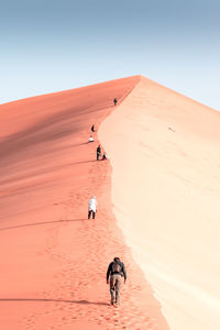 People walking on desert against clear sky