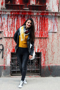 Full length portrait of young woman standing against splattered wall