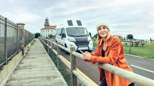 Woman looking camera leaning on fence in front of camper van