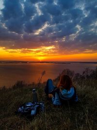 People sitting on land by sea against sky during sunset