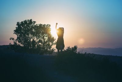 Silhouette of woman by tree against sky during sunset