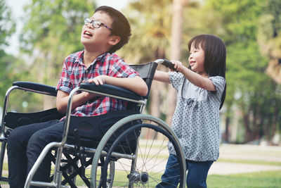 Smiling girl pushing brother on wheelchair at park