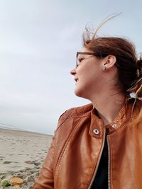 Smiling woman looking away while sitting at beach against sky