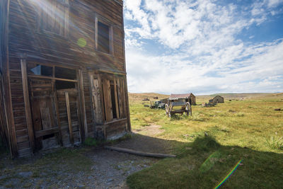 Abandoned truck near old fashioned western building made of wood on field against sky