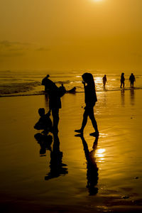 Silhouette people on beach against sky during sunset