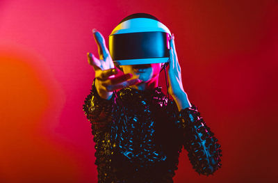 Young woman with shaved head wearing virtual reality glasses against pink background