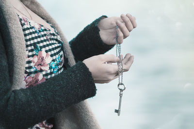 Midsection side view of young woman holding chain with key pendant at beach