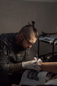 Tattooist using machine and making tattoo with black ink in salon in anonymous cropped client