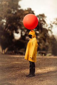 Person in hood holding balloon while standing on field