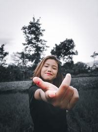 Portrait of smiling woman standing by tree against sky