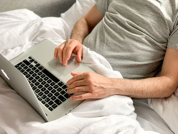 Middle aged man using laptop home bed vibes white bedsheets alone early morning working freelancer