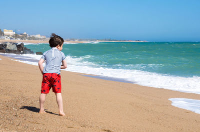 Rear view of boy on beach against sky