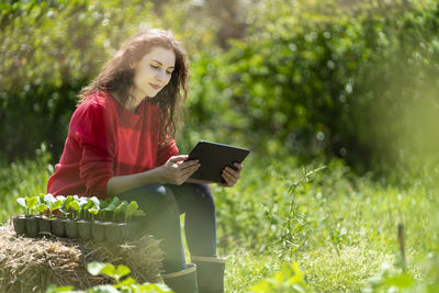 Young woman using phone while sitting on plant