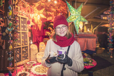 Portrait of young woman standing in illuminated christmas tree during winter