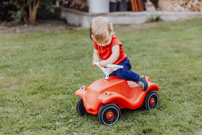 Baby girl sitting on red toy car in lawn