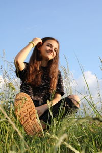 Smiling young woman sitting on field against sky