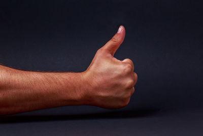 Close-up of human hand showing thumbs up sign over black background