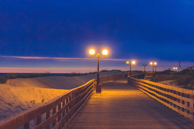 Illuminated street lights on footpath against sky at night