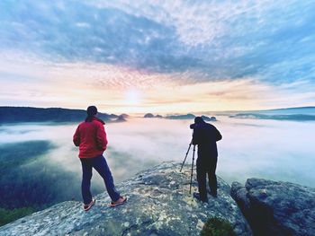 Rear view of men standing on rock against sky