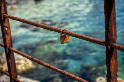 Rusty padlock hanging on railing against sea