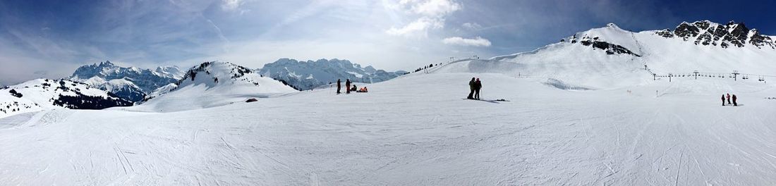 Panoramic view of people skiing on snowcapped mountain against sky