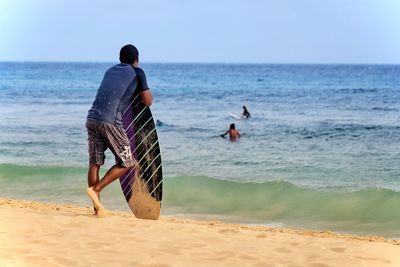 Rear view of men at beach against sky