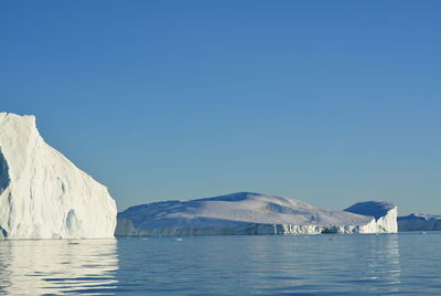 Scenic view of sea and snowcapped mountains against clear blue sky