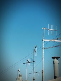 Low angle view of electricity pylon against clear blue sky