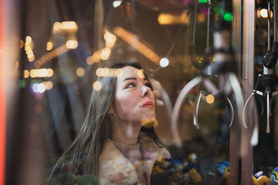 Woman looking at game machine seen through glass