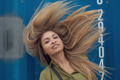 Portrait of smiling young woman tossing hair against blue metal