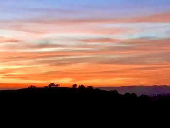 Silhouette landscape against dramatic sky during sunset