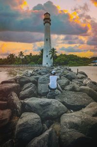 Lighthouse by sea against sky during sunset