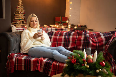 Smiling young woman using mobile phone while sitting on sofa at home