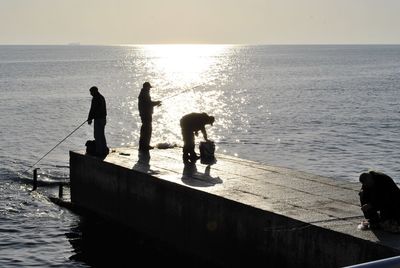 Silhouette men fishing on pier in sea during sunset