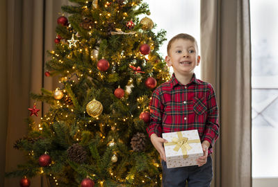 Portrait of young woman standing by christmas tree at home