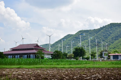 Traditional windmill on field by houses against sky