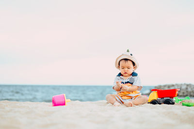 Cute boy sitting on toy at beach against sky