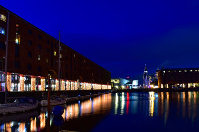 Illuminated buildings by river against sky at night