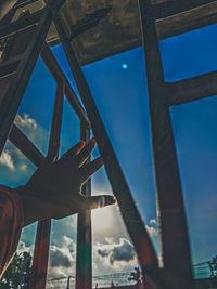 Close-up of hand against sky seen through window