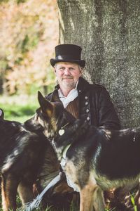 Portrait of man with dogs against tree trunk