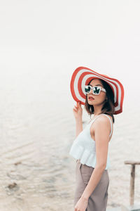 Side view of young woman wearing sunglasses standing against sea