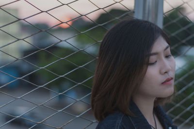 Young woman standing against chainlink fence