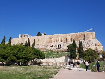 People at historical building against clear blue sky